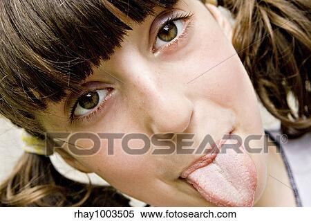 Stock Photography - The brown-eyed dark-haired girl-teenager looks directly in a shot and puts out the tongue The brown-eyed dark-haired girl-teenager looks directly in a shot and puts out the tongue . Fotosearch