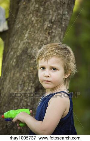Stock Photo - The little girl in a dark blue dress is going to shoot from a water pistol in summer dayThe little girl in a dark blue dress is going to shoot from a water pistol in summer day. Fotosearch
