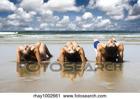 Stock Image - Three best friends seated on the sand having fun on the beach. Fotosearch