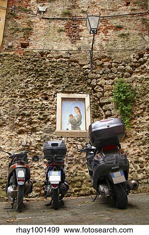 Stock Photo - Three scooters parked in an Iatlian alley in front of a generic painting of Mary and the child Jesus. Perfect image of the old and modern Italy unified.. Fotosearch