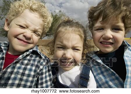 Stock Image - Triplets make faces in a wide angle portrait. Fotosearch