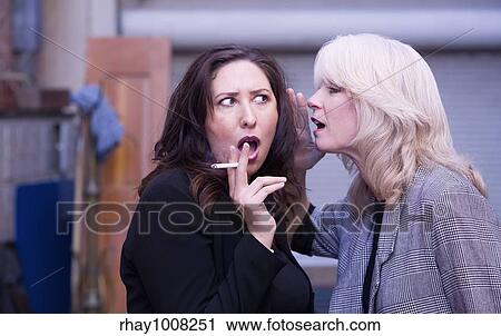 Stock Image - Two women engaging in gossip during a smoking break. Fotosearch