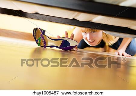 Stock Photo - woman looking for her shoe under the bed. Fotosearch