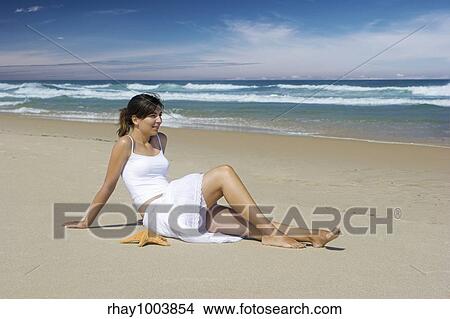 Picture - Woman on a beautiful beach with a starfish on the sand. Fotosearch