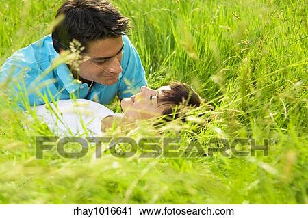 Stock Image - young couple laying down in meadow and hugging. Fotosearch