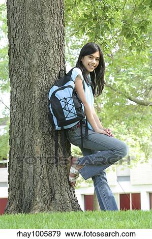 Stock Photo - "Young teen girl standing with backpack by tree, smiling. Part asian, Scandinavian descent. ". Fotosearch