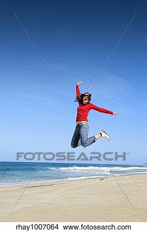 Picture - Young woman jumping on the beach and having fun. Fotosearch