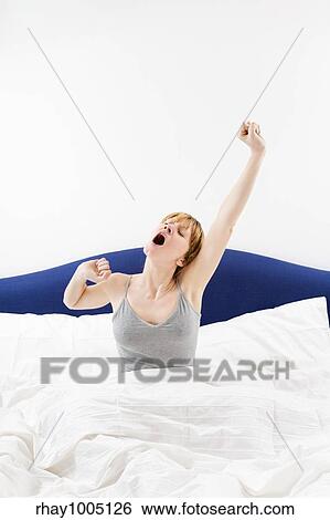"Young woman sitting on bed, stretching arms above head and yawning" View Large Photo Image Stock Photograph - "Young woman sitting on bed, stretching arms above head and yawning". Fotosearch