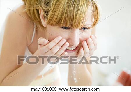 Stock Image - young woman washing her face in a basin and looking herself at the mirror. Fotosearch