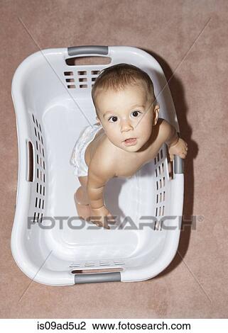Stock Image - Baby girl standing in laundry basket, high angle. Fotosearch