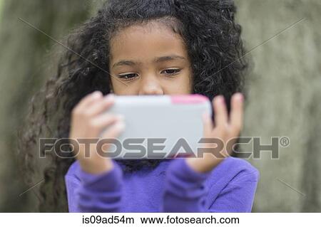 Picture - Close up of young girl in park playing hand held video game. Fotosearch