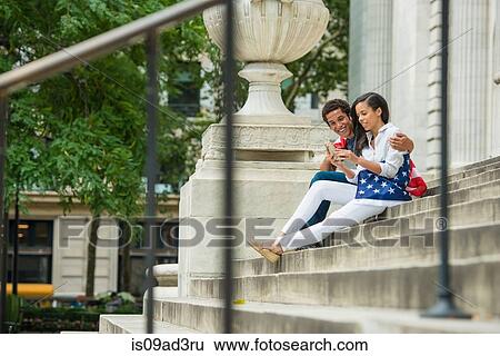 Couple looking at photograph in mobile phone View Large Photo Image Stock Photograph - Couple looking at photograph in mobile phone. Fotosearch