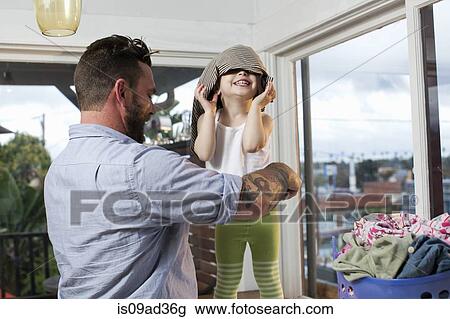 Stock Image - Father and toddler sorting laundry, toddler with clothes on her head. Fotosearch