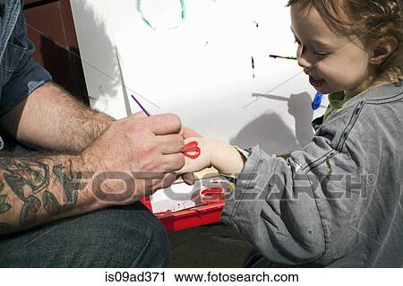 Stock Image - Father painting heart shape on daughter's hand. Fotosearch