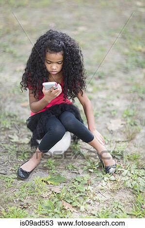 Girl sitting in park looking at hand held video game View Large Photo Image Stock Image - Girl sitting in park looking at hand held video game. Fotosearch