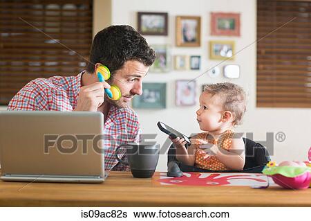 Man and baby sitting at kitchen counter playing with smartphone and toy phone View Large Photo Image Stock Photograph - Man and baby sitting at kitchen counter playing with smartphone and toy phone. Fotosearch