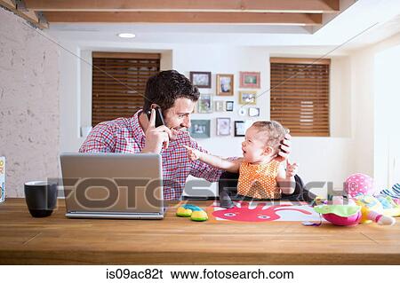 Stock Photograph - Man and baby sitting at kitchen counter making phone call. Fotosearch
