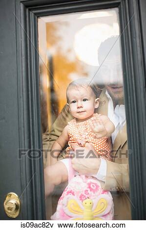 Stock Photo - Man holding baby looking through front door. Fotosearch