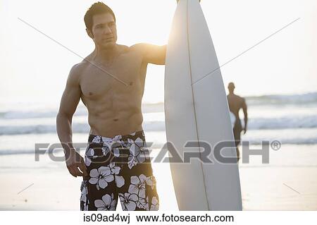 Man holding surfboard on beach View Large Photo Image Stock Image - Man holding surfboard on beach. Fotosearch