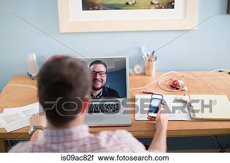 Stock Image - Man sitting at desk making video call. Fotosearch