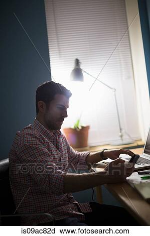 Man sitting at desk using smartphone View Large Photo Image Stock Image - Man sitting at desk using smartphone. Fotosearch