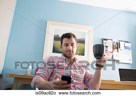 Man sitting at desk with smartphone and coffee cup View Large Photo Image Picture - Man sitting at desk with smartphone and coffee cup. Fotosearch