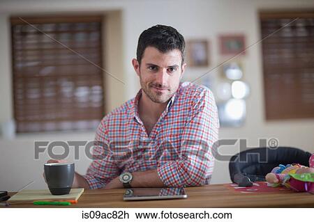 Stock Image - Man sitting at kitchen counter with cup of coffee and digital tablet. Fotosearch
