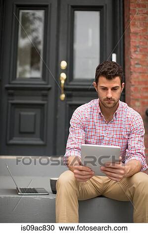Stock Image - Man sitting on step using digital tablet. Fotosearch