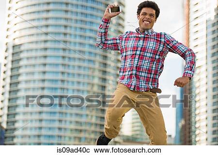 Stock Image - Man with mobile phone jumping for joy. Fotosearch