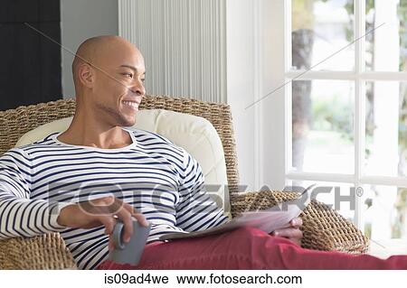 Stock Image - Mid adult man sitting in wicker chair. Fotosearch