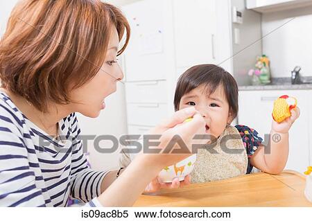Stock Photography - Mother feeding baby in kitchen. Fotosearch