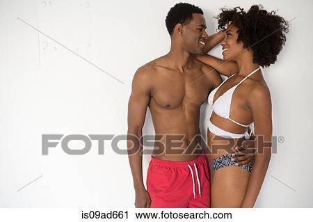 Stock Image - Portrait of young couple wearing swimwear against white background. Fotosearch