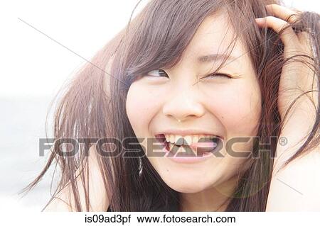 Stock Image - Portrait of young woman, hands in hair, sticking tongue out. Fotosearch