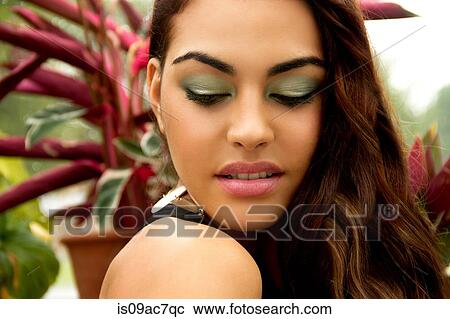 Stock Image - Portrait of young woman, wearing eye shadow, looking down. Fotosearch