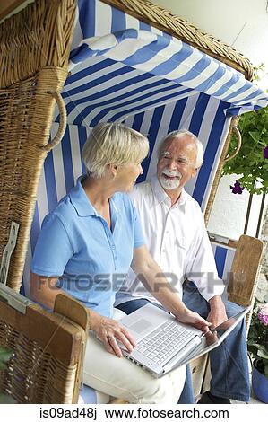 Retired couple using laptop on garden seat View Large Photo Image Stock Image - Retired couple using laptop on garden seat. Fotosearch