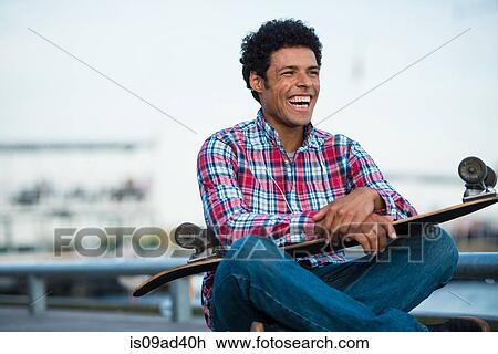 Stock Image - Skateboarder sitting with skateboard on lap. Fotosearch