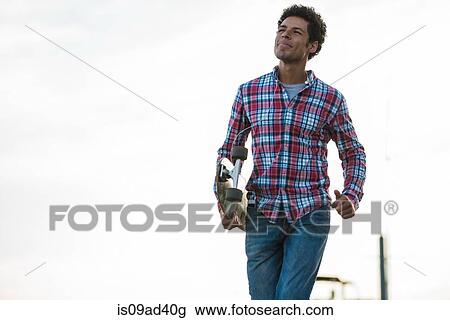 Stock Image - Skateboarder walking with skateboard in hand. Fotosearch