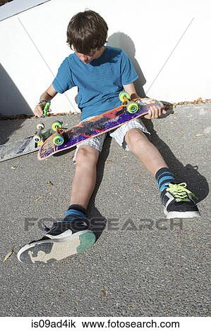 Teenage boy sitting on ground preparing skateboard View Large Photo Image Stock Image - Teenage boy sitting on ground preparing skateboard. Fotosearch