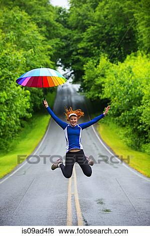 Stock Photograph - Teenage girl jumping with umbrella on road, Bainbridge Island, Washington, USA. Fotosearch