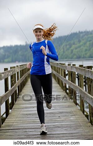 Stock Image - Teenage girl running on pier, Bainbridge Island, Washington, USA. Fotosearch