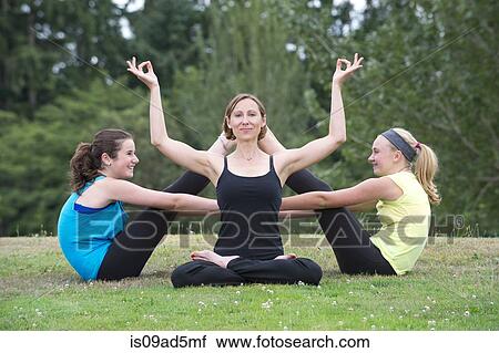 Stock Image - Teenage girls and yoga tutor sitting on grass. Fotosearch