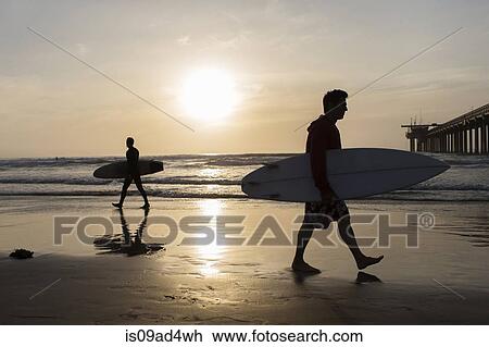 Stock Image - Two men carrying surfboards on beach. Fotosearch