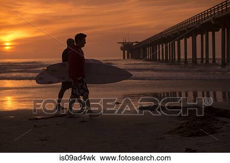 Stock Image - Two men carrying surfboards on beach. Fotosearch