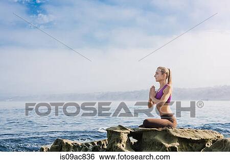 Stock Photograph - Woman doing yoga at coast. Fotosearch