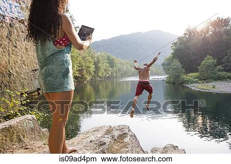 Woman photographing boyfriend jumping from rock ledge, Hamburg, Pennsylvania, USA View Large Photo Image Picture - Woman photographing boyfriend jumping from rock ledge, Hamburg, Pennsylvania, USA. Fotosearch