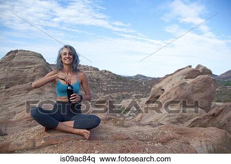 Stock Photography - Woman sitting at Vazquez Rocks, opening drinks bottle. Fotosearch