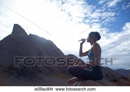 Stock Photograph - Woman sitting cross legged at Vazquez Rocks, drinking bottle of water. Fotosearch