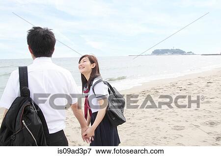 Stock Photo - Young couple holding hands on beach, rear view. Fotosearch