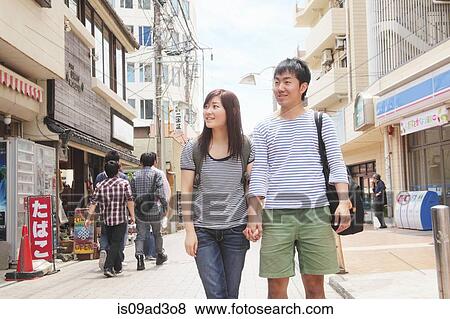 Stock Photo - Young couple holding hands walking through Kamakura, Japan. Fotosearch