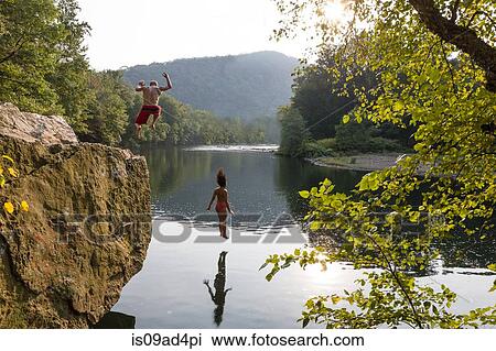 Stock Image - Young couple jumping from rock ledge, Hamburg, Pennsylvania, USA. Fotosearch